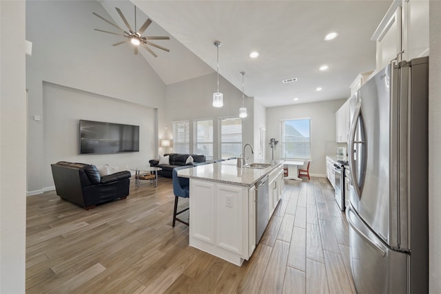 kitchen featuring appliances with stainless steel finishes, decorative light fixtures, light hardwood / wood-style flooring, white cabinetry, and an island with sink