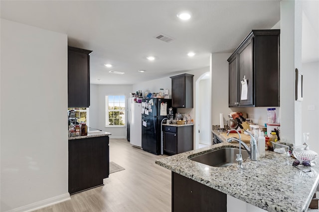 kitchen with black fridge, sink, light hardwood / wood-style flooring, light stone countertops, and kitchen peninsula