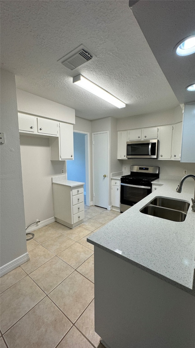 kitchen featuring white cabinets, sink, a textured ceiling, appliances with stainless steel finishes, and light tile patterned flooring