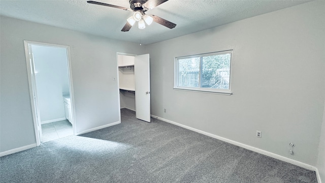 unfurnished bedroom with a textured ceiling, a walk in closet, dark carpet, and ceiling fan