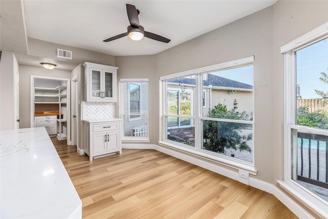 interior space featuring white cabinetry, backsplash, ceiling fan, light stone countertops, and light hardwood / wood-style flooring