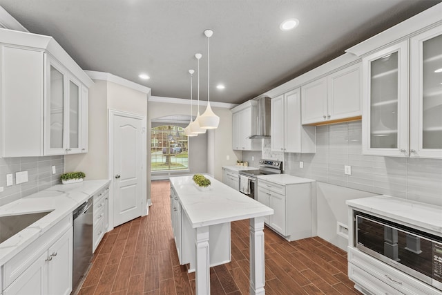 kitchen featuring appliances with stainless steel finishes, wall chimney exhaust hood, dark wood-type flooring, pendant lighting, and white cabinetry