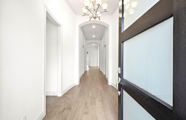 hallway featuring light hardwood / wood-style flooring, ornamental molding, and a notable chandelier