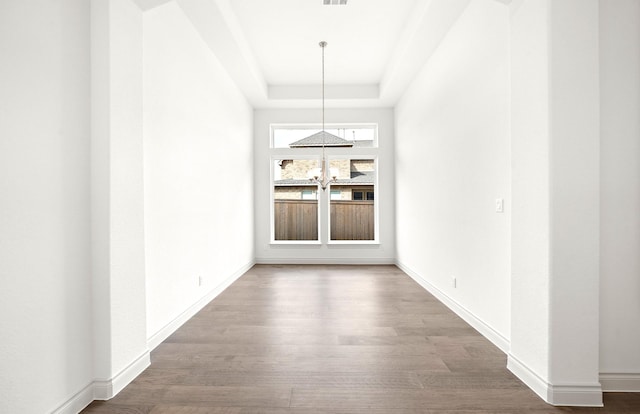 unfurnished dining area with wood-type flooring, a tray ceiling, and a chandelier