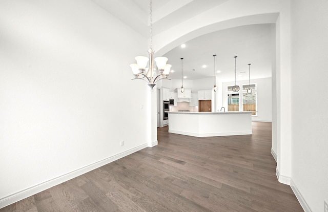 interior space with pendant lighting, a center island with sink, white cabinets, dark hardwood / wood-style floors, and a chandelier