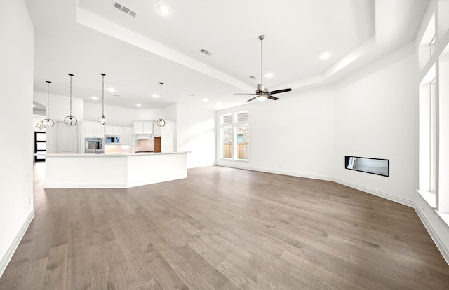 unfurnished living room with a tray ceiling, light hardwood / wood-style flooring, and ceiling fan