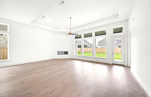 unfurnished living room with a tray ceiling, light hardwood / wood-style flooring, and ceiling fan