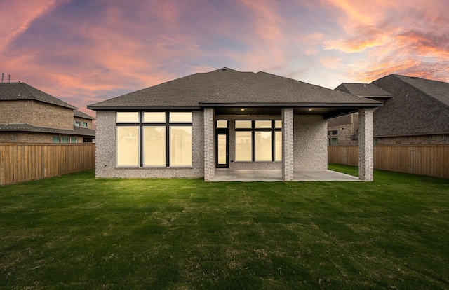 back house at dusk with a lawn and a patio area