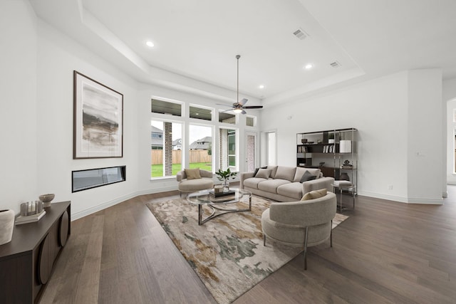 living room featuring a raised ceiling, ceiling fan, and dark wood-type flooring