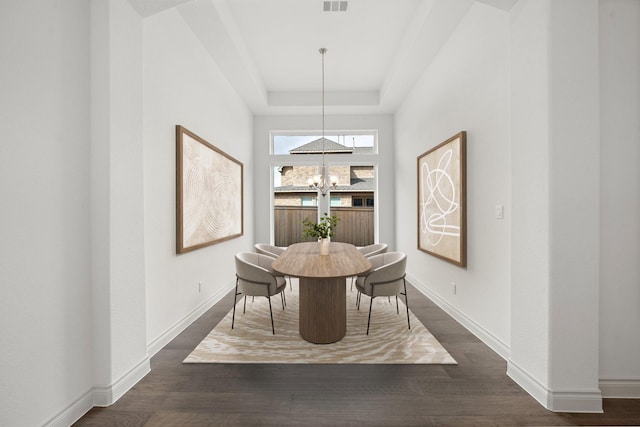 dining space with a raised ceiling, dark hardwood / wood-style flooring, and a notable chandelier