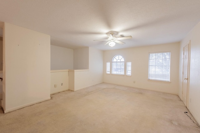 empty room with ceiling fan, light colored carpet, and a textured ceiling