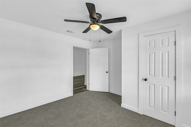 unfurnished bedroom featuring a closet, dark carpet, ceiling fan, and a textured ceiling