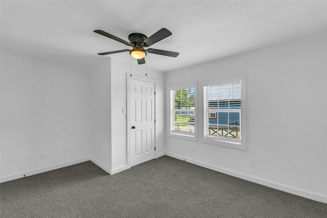 unfurnished room with a textured ceiling, dark carpet, and ceiling fan