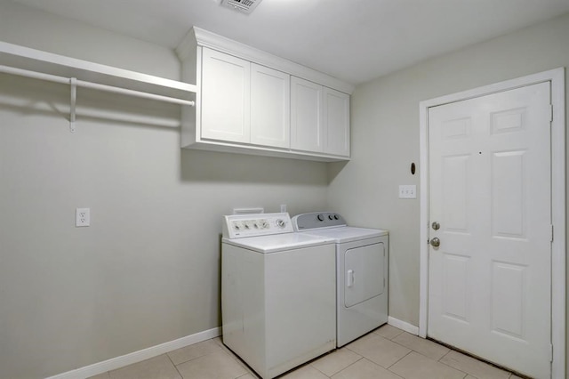 clothes washing area featuring washer and dryer, light tile patterned floors, and cabinets