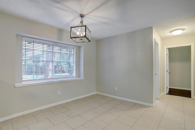 empty room with a textured ceiling, light tile patterned flooring, and an inviting chandelier