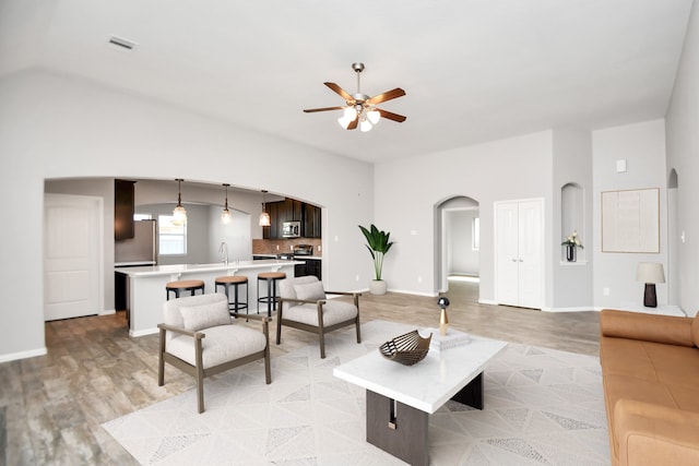 living room featuring vaulted ceiling, sink, ceiling fan, and light wood-type flooring