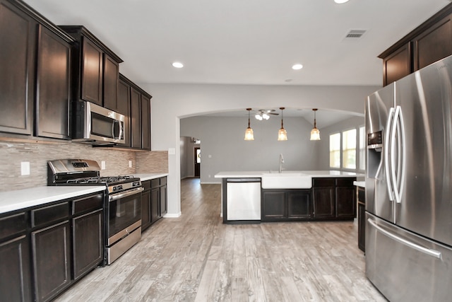 kitchen with dark brown cabinetry, stainless steel appliances, decorative light fixtures, and light wood-type flooring