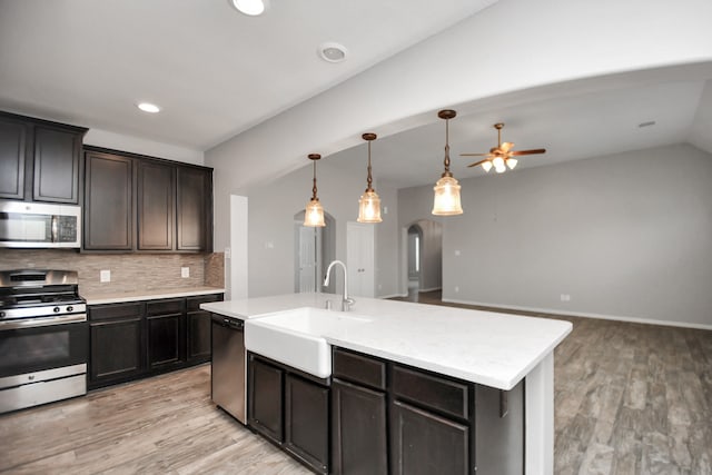 kitchen featuring sink, stainless steel appliances, tasteful backsplash, light hardwood / wood-style flooring, and an island with sink