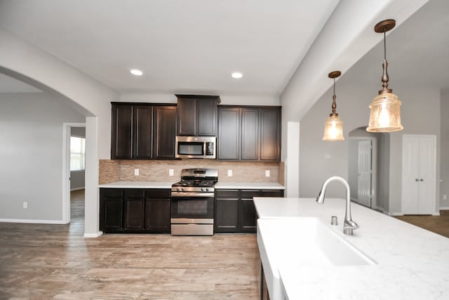 kitchen with sink, hanging light fixtures, appliances with stainless steel finishes, light hardwood / wood-style floors, and dark brown cabinetry