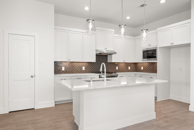 kitchen with white cabinetry, stainless steel microwave, an island with sink, and pendant lighting