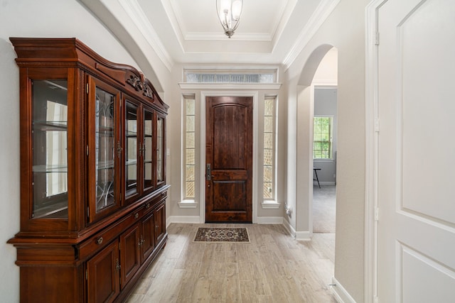 foyer entrance featuring a raised ceiling, ornamental molding, and light wood-type flooring