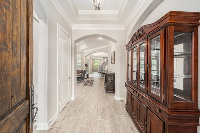 hall featuring a tray ceiling, crown molding, and light wood-type flooring