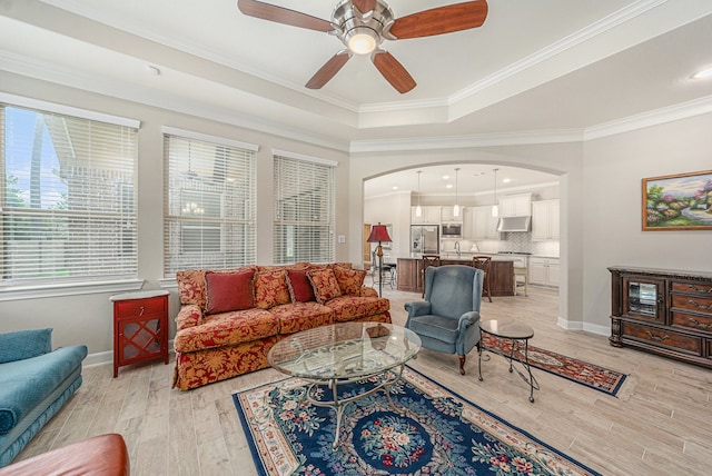 living room with ceiling fan, light hardwood / wood-style floors, crown molding, and a tray ceiling