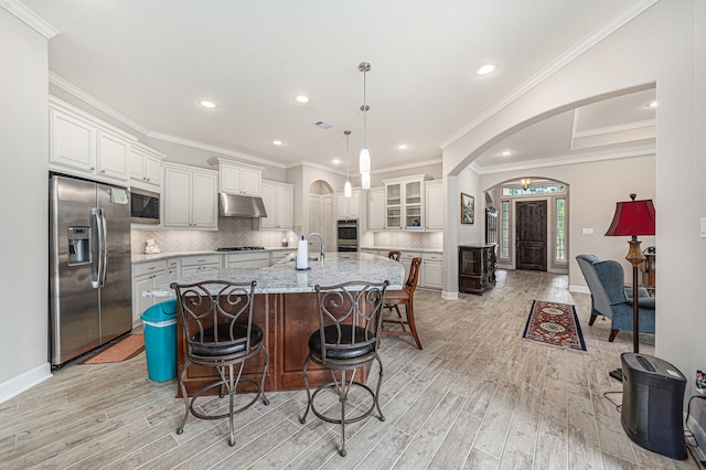 kitchen with light stone countertops, hanging light fixtures, stainless steel appliances, a center island with sink, and light wood-type flooring