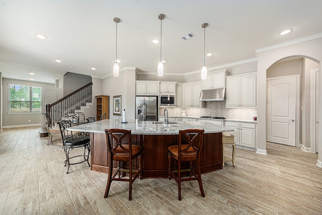 kitchen featuring stainless steel appliances, sink, a large island with sink, decorative light fixtures, and light hardwood / wood-style flooring