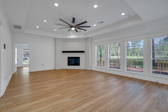 unfurnished living room with a tray ceiling, ceiling fan, and light wood-type flooring