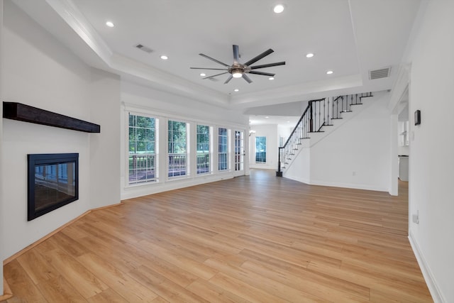 unfurnished living room featuring a raised ceiling, ceiling fan, and light hardwood / wood-style floors