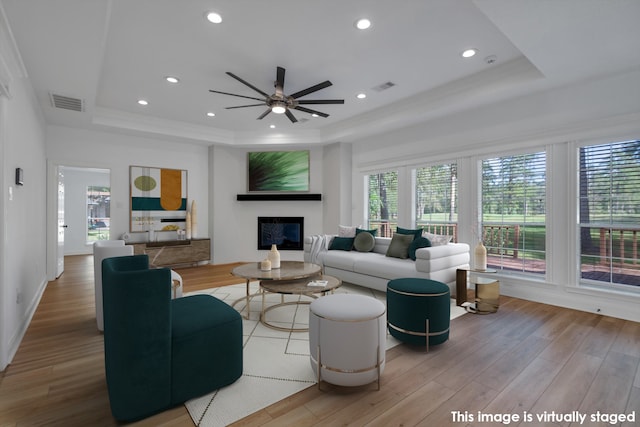 living room with a raised ceiling, ceiling fan, and light hardwood / wood-style flooring