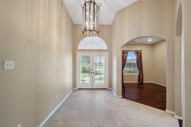 entrance foyer with french doors, light hardwood / wood-style floors, high vaulted ceiling, and a notable chandelier