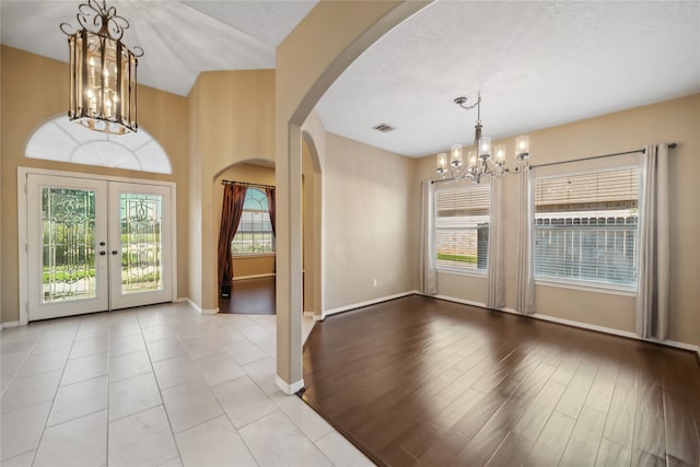 entryway with french doors, a textured ceiling, light hardwood / wood-style floors, and an inviting chandelier