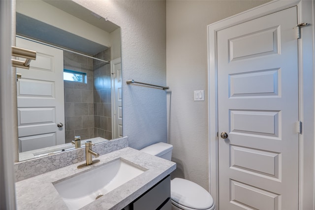 bathroom featuring a tile shower, vanity, and toilet