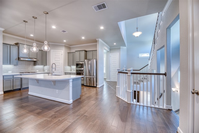 kitchen featuring dark hardwood / wood-style floors, decorative light fixtures, a kitchen bar, a center island with sink, and appliances with stainless steel finishes