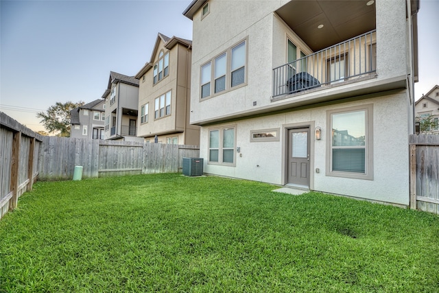 rear view of property featuring central air condition unit and a lawn