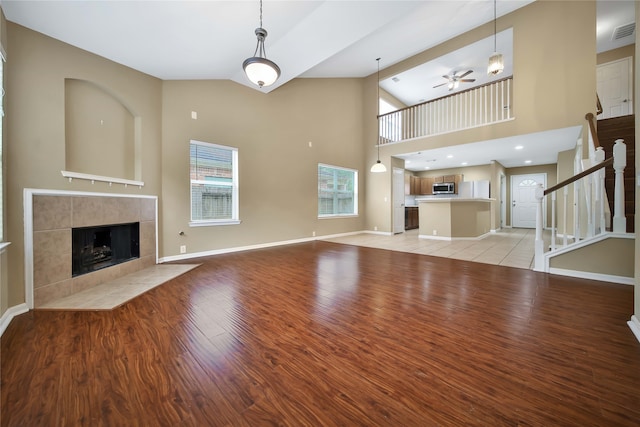 unfurnished living room featuring high vaulted ceiling, ceiling fan, a tiled fireplace, and light wood-type flooring