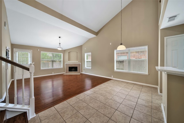 unfurnished living room with a tiled fireplace, high vaulted ceiling, and light wood-type flooring