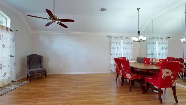 dining space with ceiling fan with notable chandelier, lofted ceiling, light wood-type flooring, and crown molding