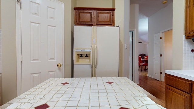 kitchen with light hardwood / wood-style floors, backsplash, white refrigerator with ice dispenser, and tile counters