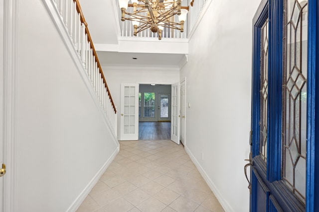 foyer with french doors, a towering ceiling, crown molding, a chandelier, and light hardwood / wood-style floors