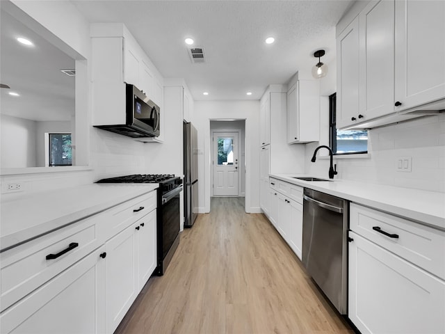 kitchen with white cabinetry, sink, tasteful backsplash, light hardwood / wood-style floors, and appliances with stainless steel finishes