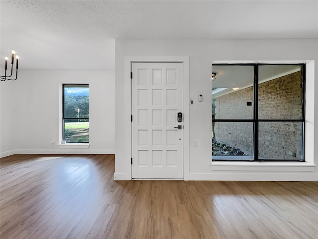 foyer entrance with an inviting chandelier, a textured ceiling, and light wood-type flooring