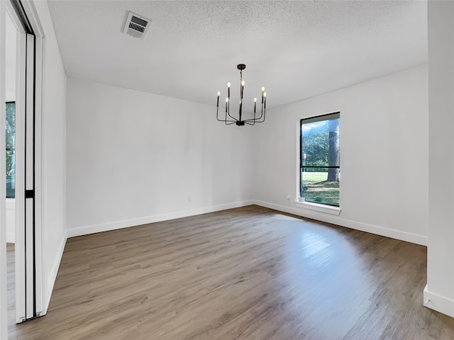 unfurnished dining area featuring light hardwood / wood-style flooring, a notable chandelier, and a textured ceiling