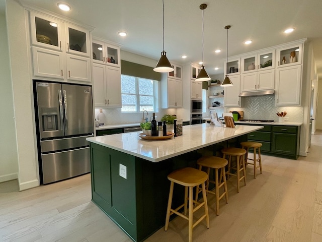 kitchen featuring light wood-type flooring, stainless steel appliances, decorative light fixtures, white cabinets, and a center island