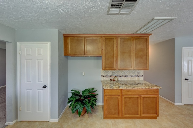 kitchen featuring light tile patterned flooring, backsplash, light stone counters, and a textured ceiling