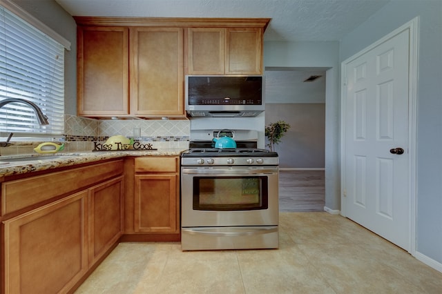 kitchen featuring decorative backsplash, appliances with stainless steel finishes, light stone counters, sink, and light tile patterned floors