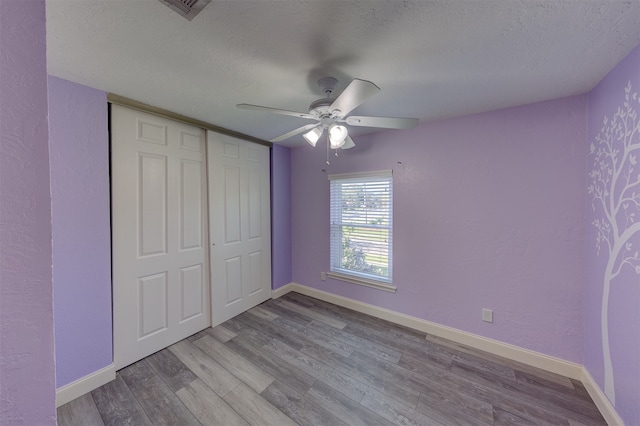 unfurnished bedroom with ceiling fan, a closet, light hardwood / wood-style floors, and a textured ceiling