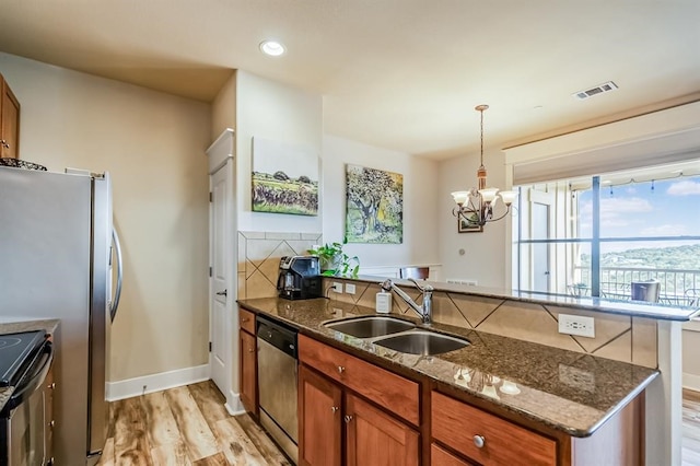 kitchen featuring appliances with stainless steel finishes, light wood-type flooring, sink, a notable chandelier, and dark stone countertops